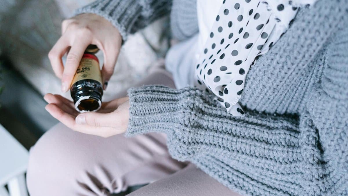 Close-up of a woman in cozy clothing holding a medicine bottle in her hands.