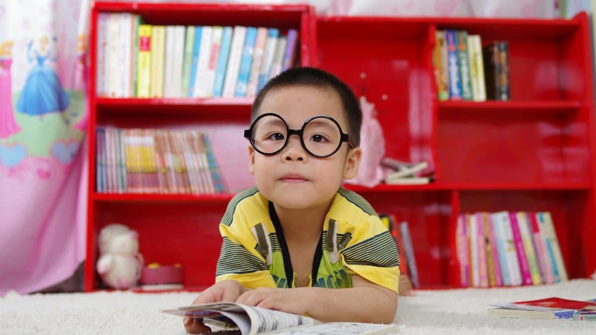 A cute child in glasses reading a book, surrounded by colorful shelves. Perfect shot of childhood learning indoors.