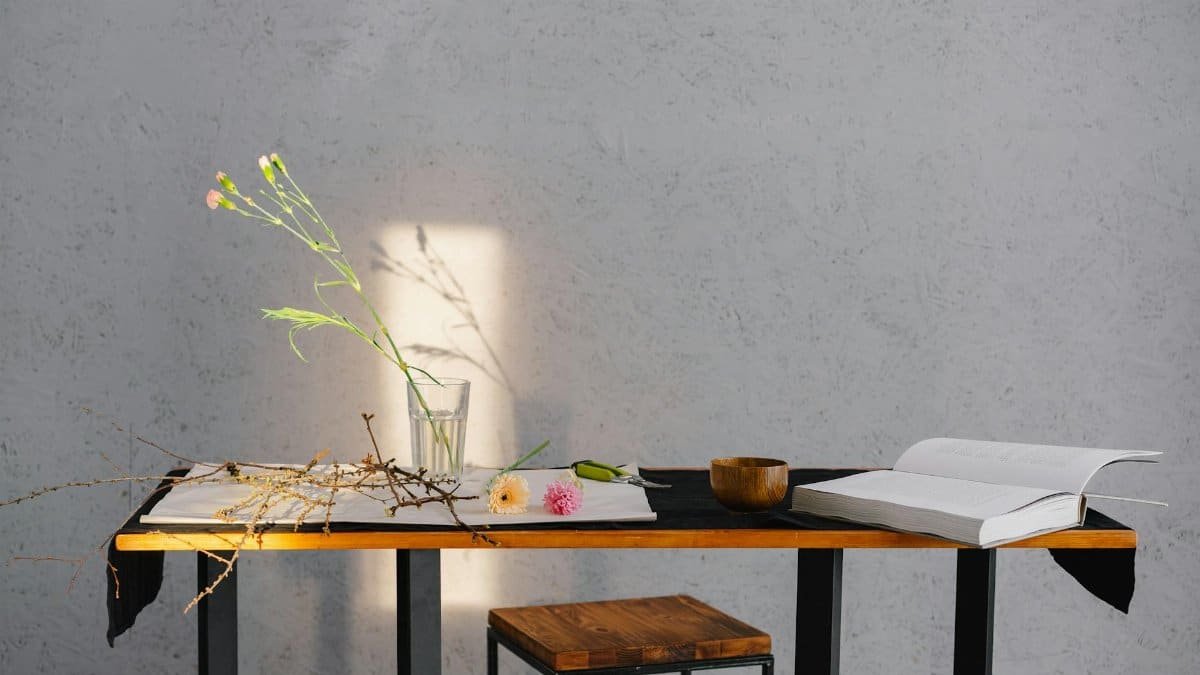 A minimalist scene of a table with flowers, an open book, and wooden bowl, enhanced by natural lighting.