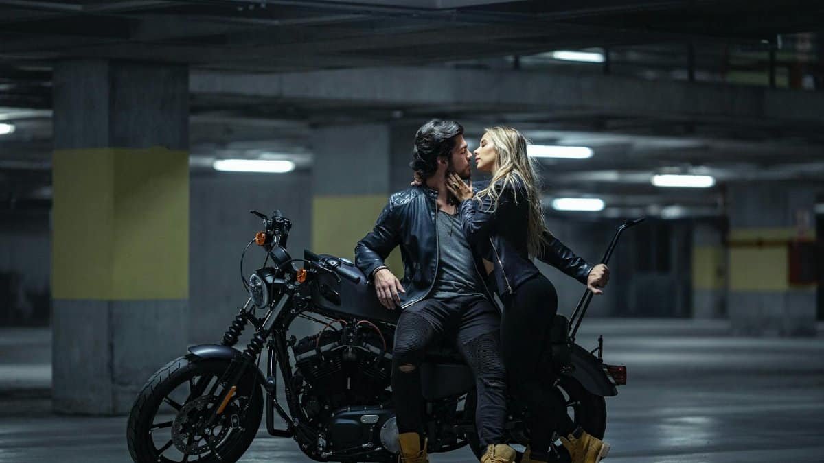 A couple embraces on a motorcycle in an underground parking garage, evoking a sense of adventure.
