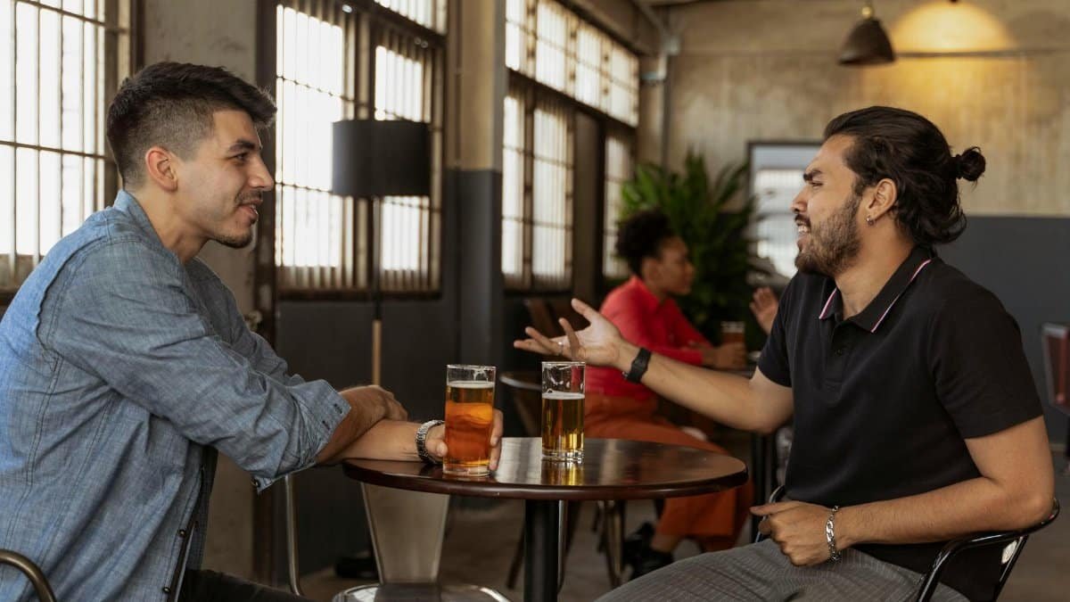 Two men engaging in a friendly conversation over beer at an indoor cafe setting.