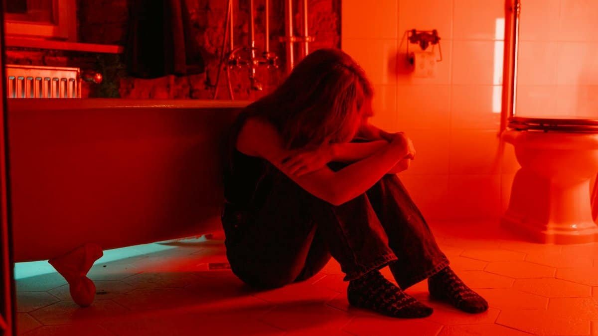 A woman sits alone in a red-lit bathroom, conveying emotions of loneliness and introspection.