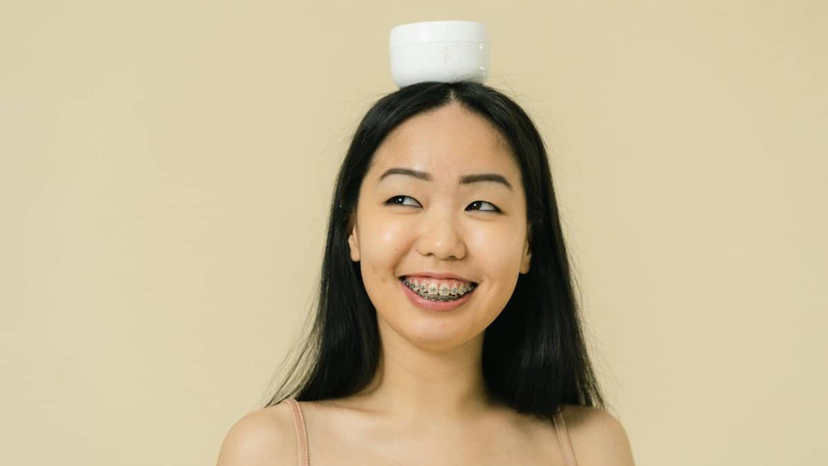 Smiling woman balancing a skincare jar on her head, captured in a studio setting.