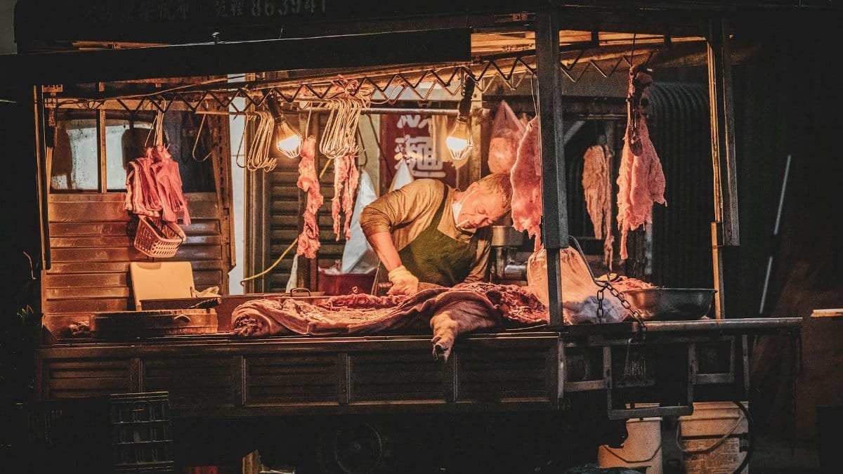 A butcher expertly cuts meat under warm lights at an outdoor night market stall.