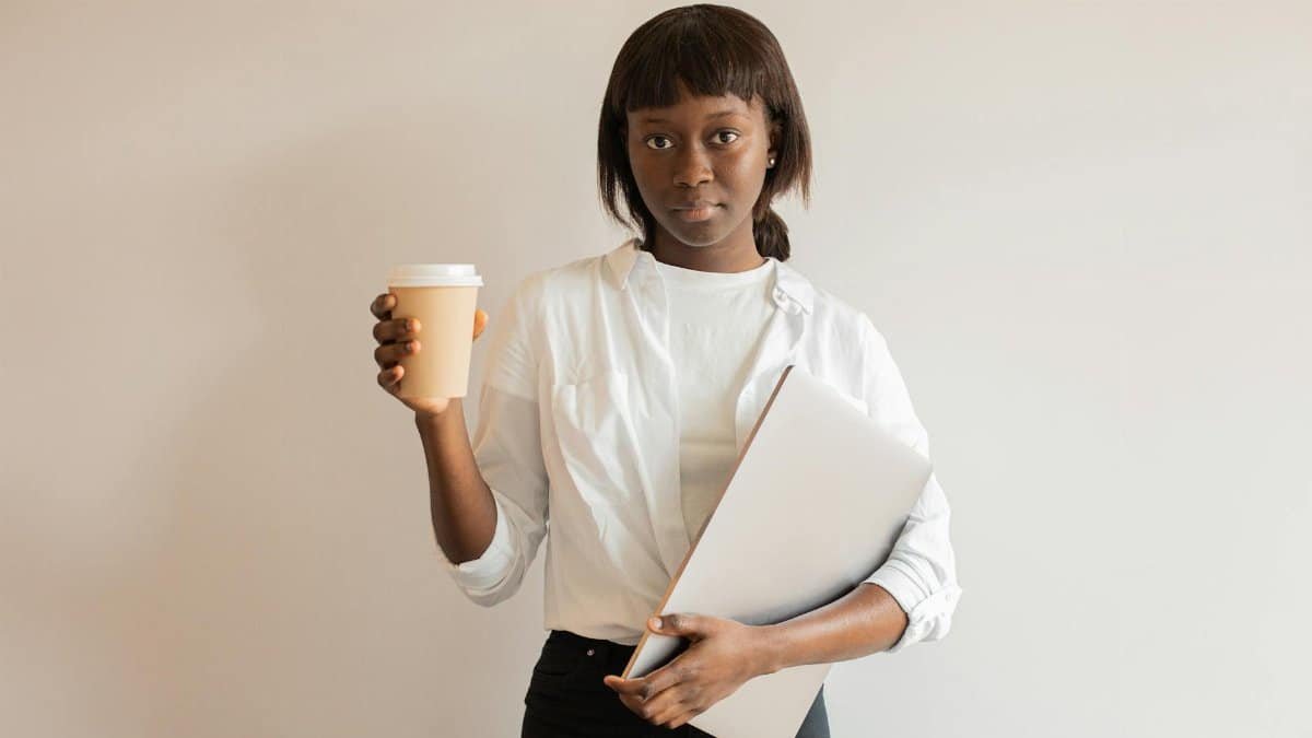 Professional woman holding disposable cup and laptop in medium close-up indoors.