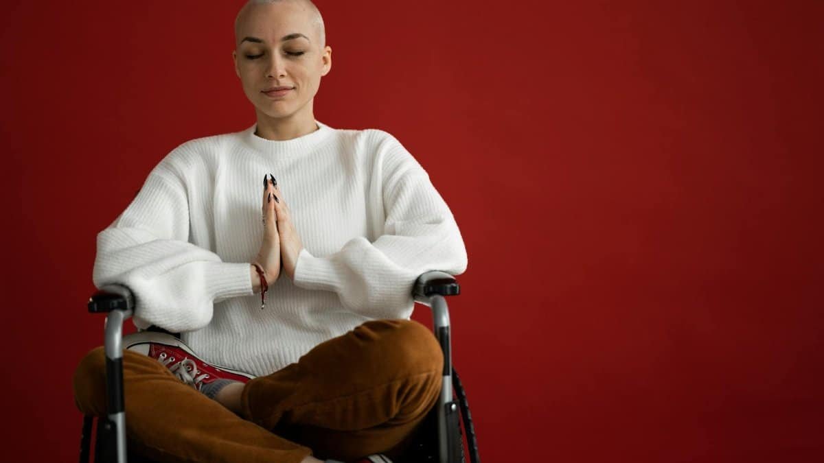 Young concentrated female with praying hands and crossed legs meditating during cancer recovery process on red background