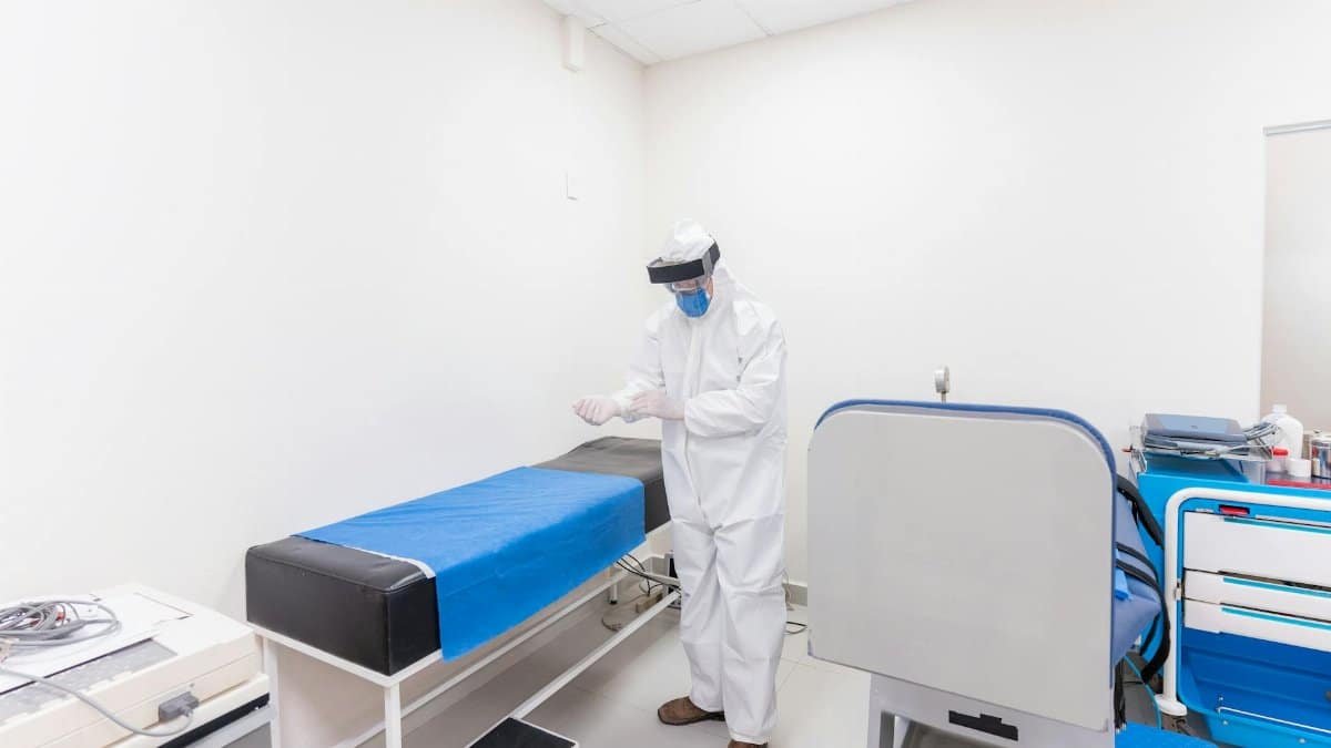 A healthcare worker in full PPE readies for work in a well-equipped hospital room.