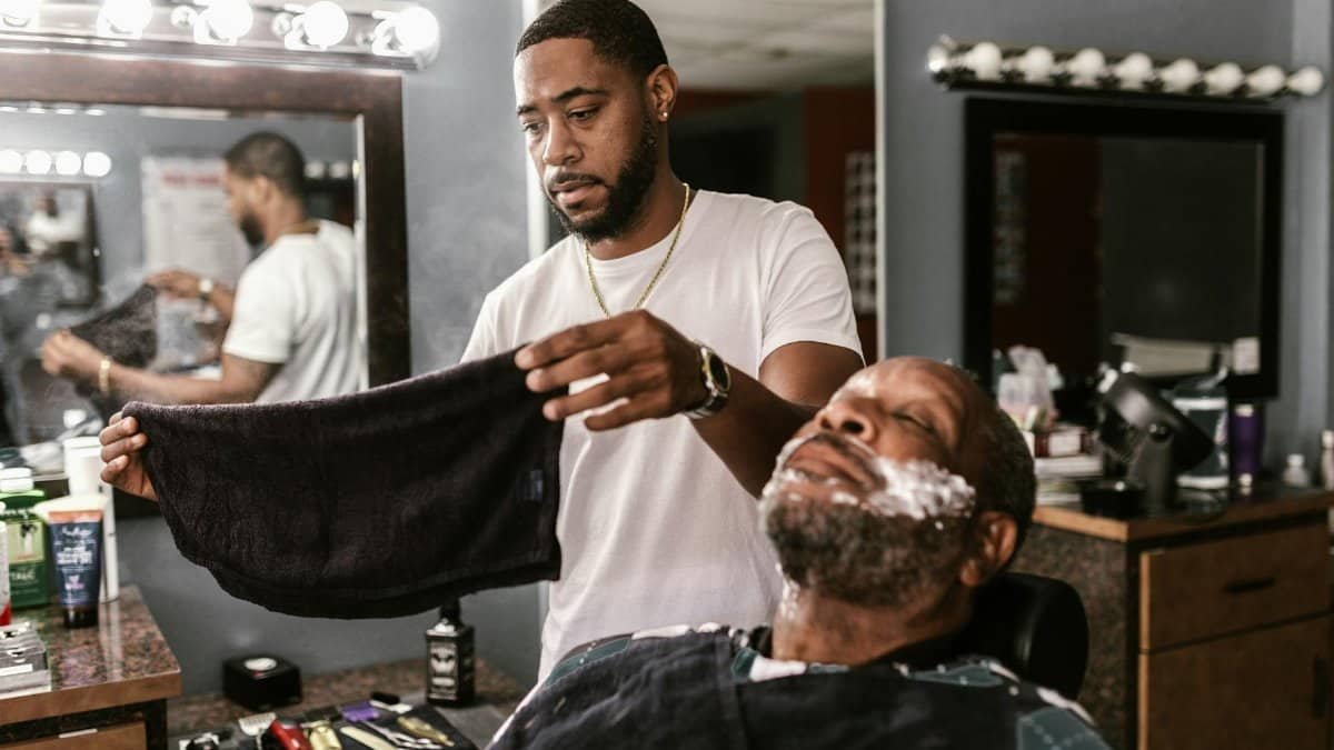 Barber prepares to shave a man with a towel in a modern barbershop.