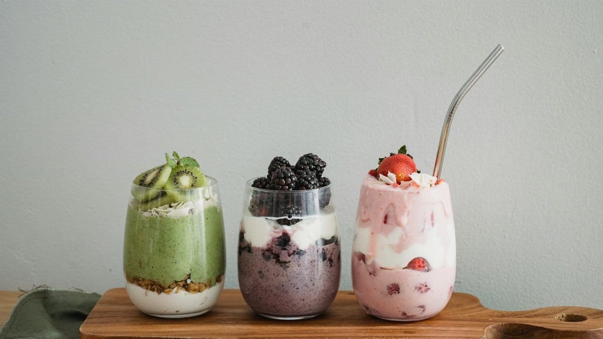 Colorful homemade fruit smoothies with kiwi, blackberry, and strawberry on a wooden board.