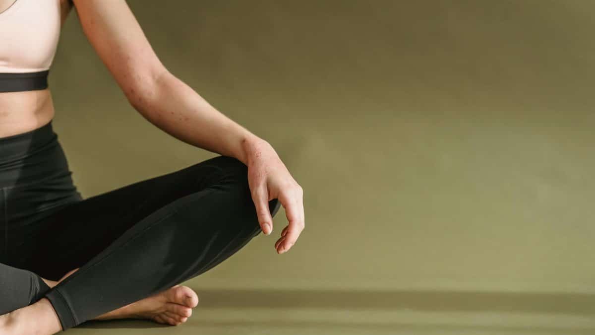 Crop unrecognizable slim female in sportswear sitting on floor and stretching legs while doing yoga in studio