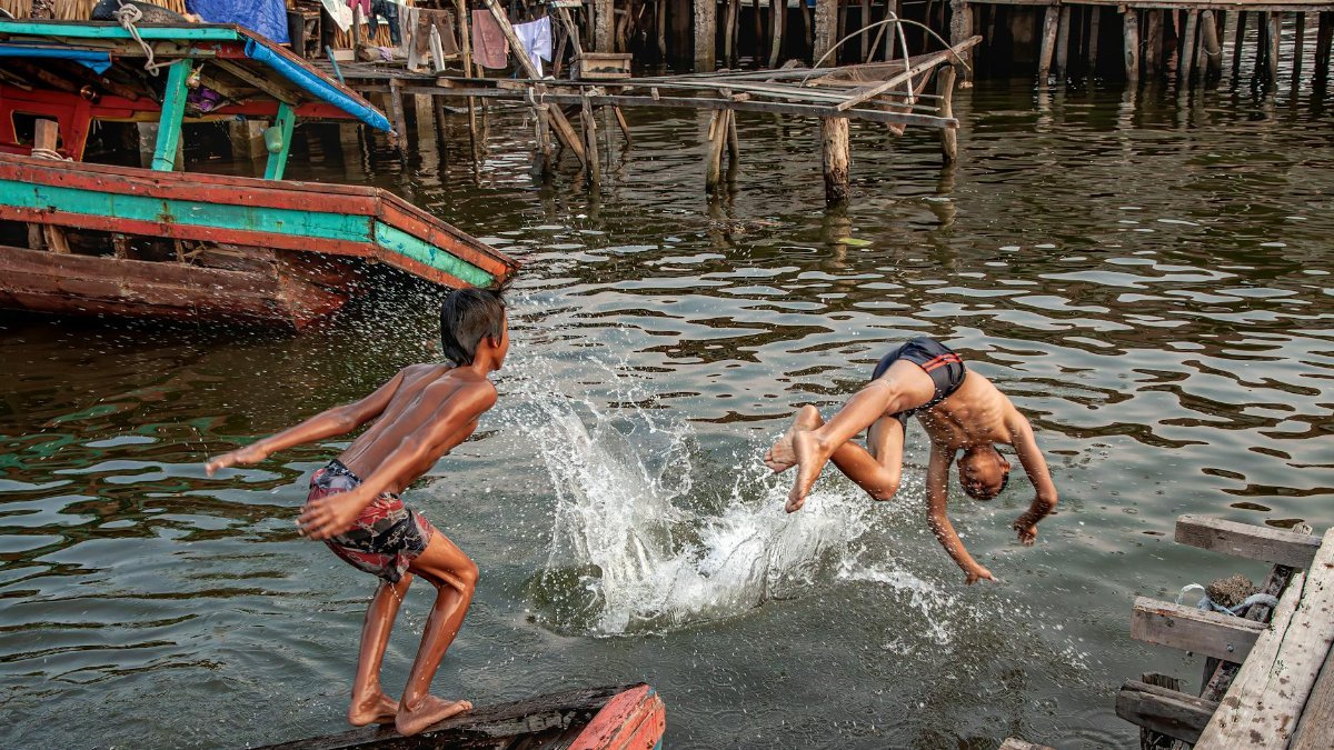 Two boys joyfully dive into water from a wooden dock, capturing a sense of summer fun and adventure.