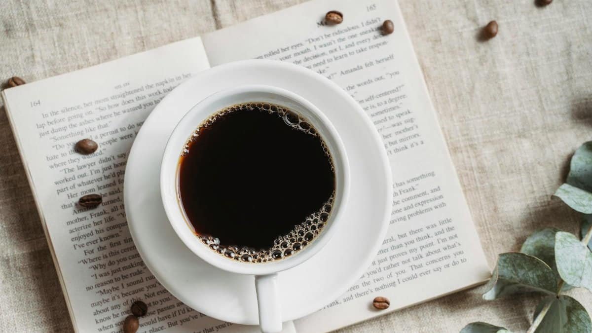 A relaxing setup featuring a cup of black coffee on an open book with scattered coffee beans.