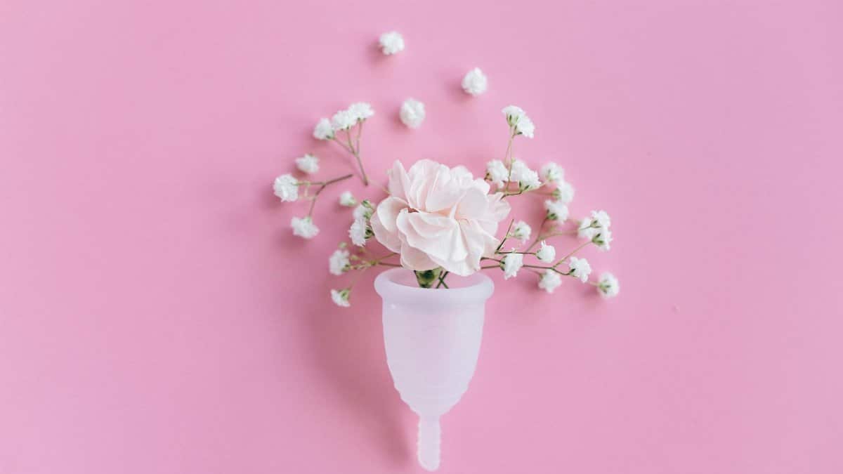 A menstrual cup filled with delicate flowers on a pink background, symbolizing feminine care and eco-friendly solutions.