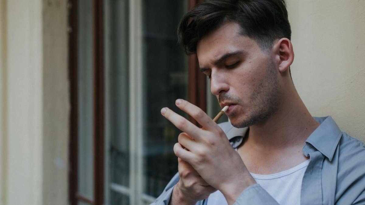Profile of a young man lighting a cigarette on a city balcony, capturing urban lifestyle.