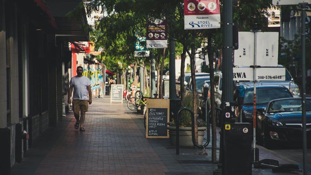 A street scene featuring a man walking on a city sidewalk with vehicles in the background.