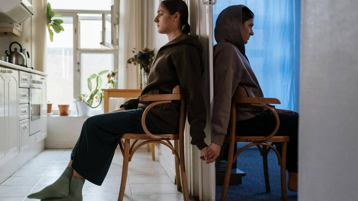 Two individuals seated back-to-back in chairs, highlighting emotion and mental health in an indoor setting.