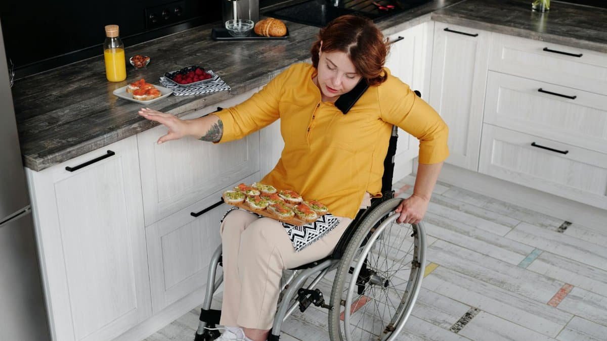 A woman in a wheelchair prepares food in a contemporary kitchen, showcasing everyday independence.
