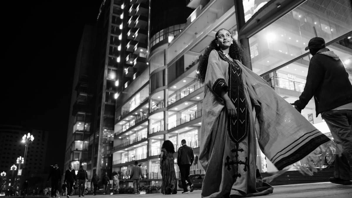 A confident woman in cultural dress stands on a bustling street in Addis Ababa at night.