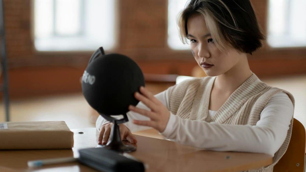 Asian woman sitting in classroom studying geography with a globe, focused on learning.