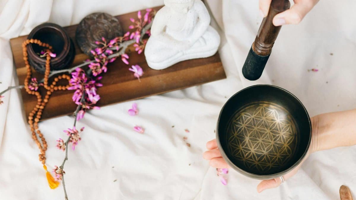 A peaceful setup with a singing bowl, flowers, and a Buddha statue for meditation.