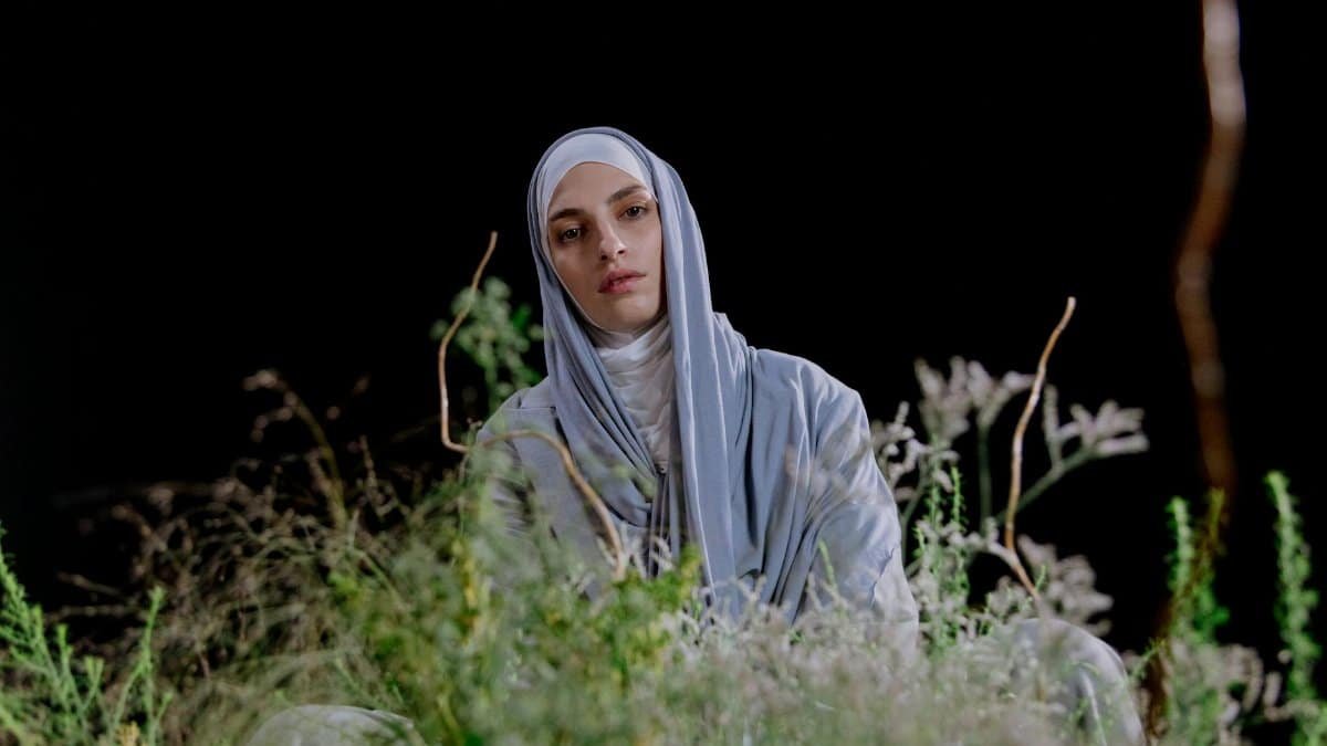 Portrait of a Muslim woman in a hijab surrounded by greenery against a black background.