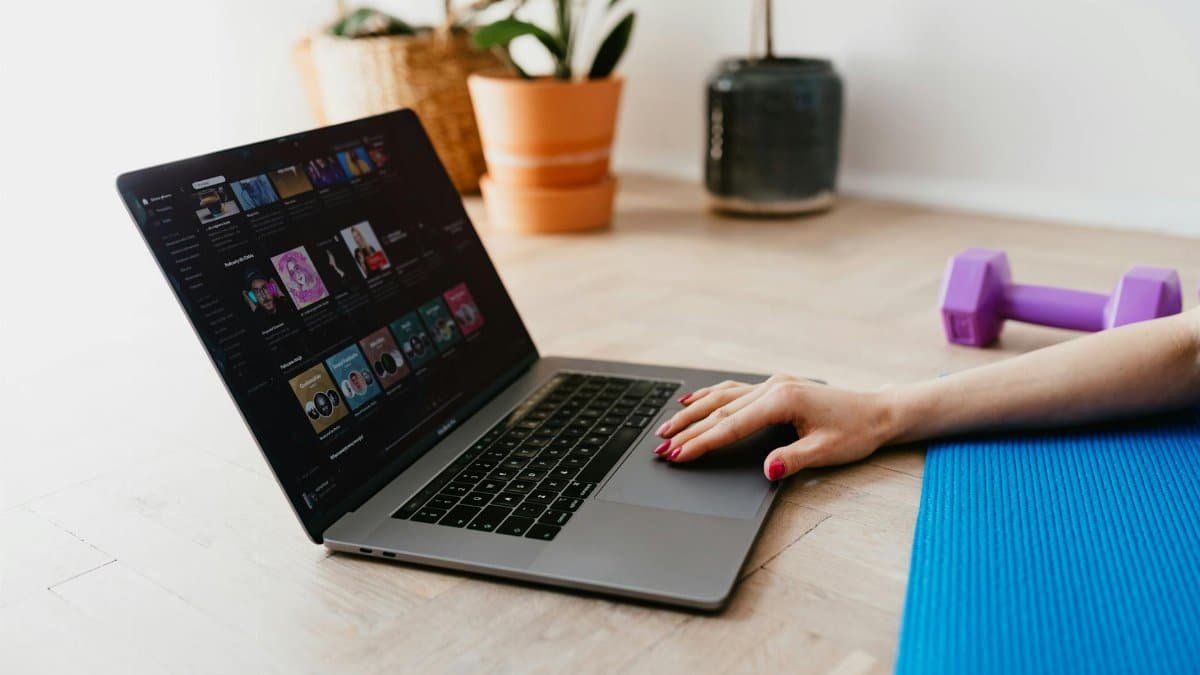 Hand of anonymous female on touchpad of laptop while surfing internet lying on mat at home during workout