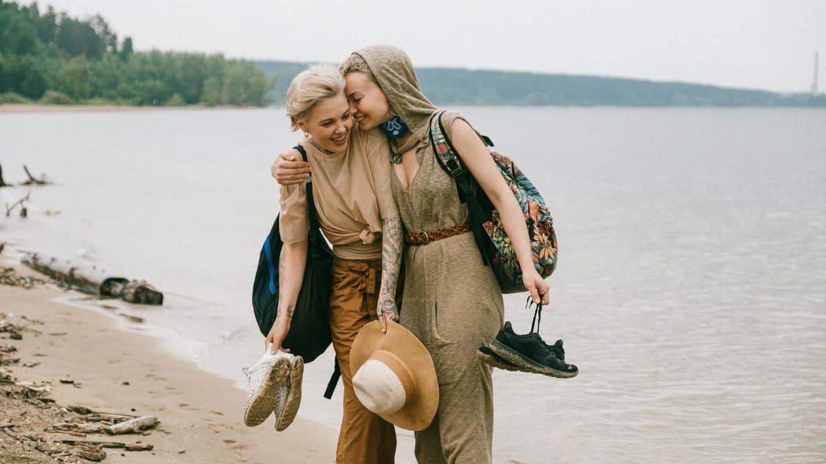 Two friends enjoy a joyful walk along the beach, embracing and smiling.