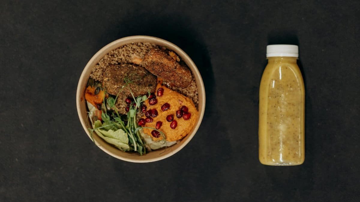 A vibrant vegan bowl with quinoa, fresh vegetables, and a smoothie bottle against a dark backdrop.