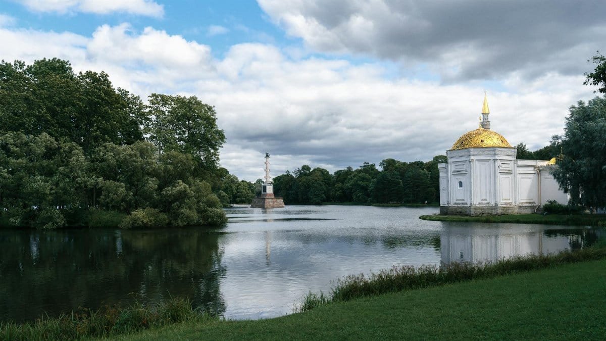 Peaceful view of a lake with a white building, golden dome, and surrounding park.