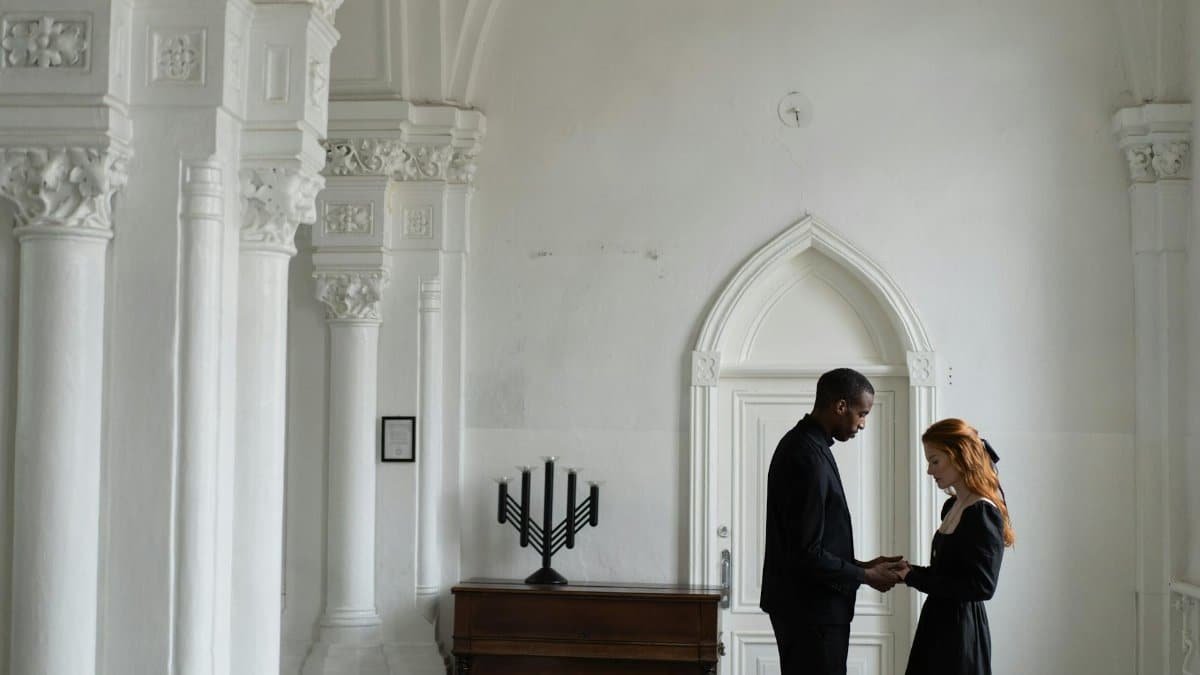 A solemn moment inside a chapel with an interracial couple praying, highlighting themes of unity and compassion.