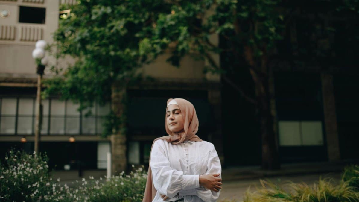 A calm woman in a hijab standing outdoors with eyes closed, exuding peace and elegance.