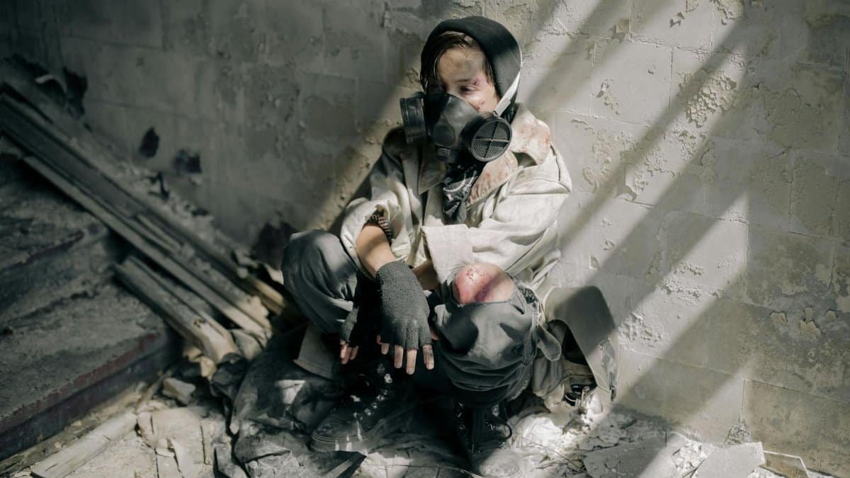 A young person in a gas mask sits in a decaying, abandoned building, evoking themes of survival and desolation.