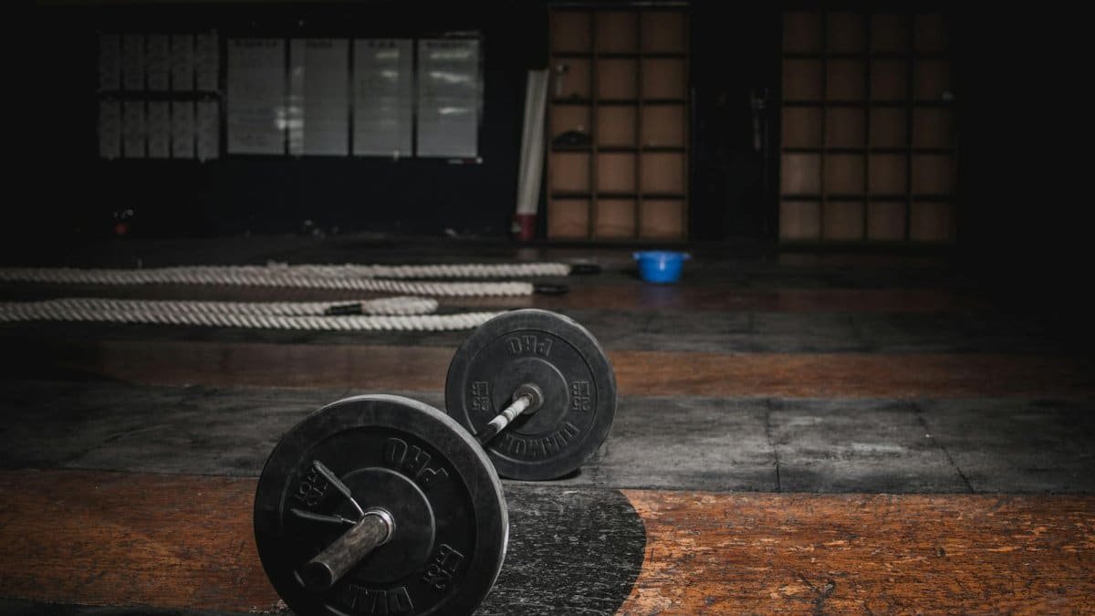 A lone barbell rests in an empty, dimly lit gym, emphasizing strength and solitude.