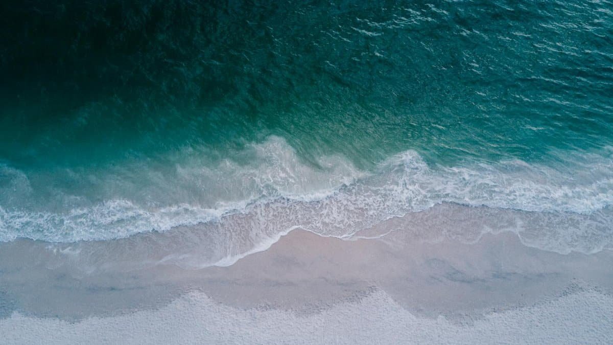 Stunning aerial shot of turquoise ocean waves washing onto a pristine sandy beach, perfect for backgrounds.