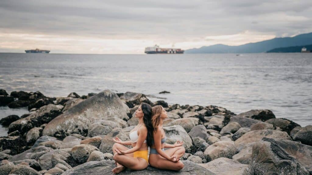 Two women meditating on a rocky coast by the ocean, embracing calmness and mindfulness.