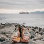 Two women meditating on a rocky coast by the ocean, embracing calmness and mindfulness.