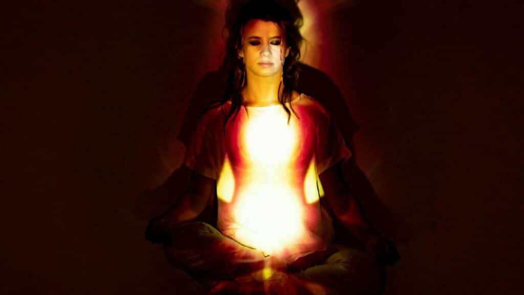 A woman in meditation surrounded by a radiant aura, symbolizing spiritual energy and enlightenment.