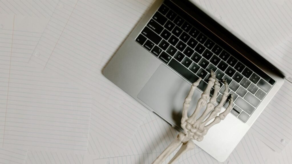Skeleton hand on laptop keyboard overlaid on papers, symbolizing burnout.