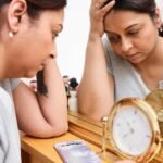 A woman looks pensive and tired, reflecting on burnout with a clock and mirror.
