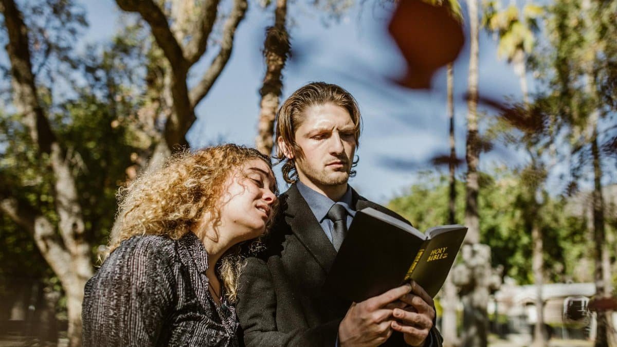 A couple standing in a cemetery, reading from the Bible, signifies faith and companionship.