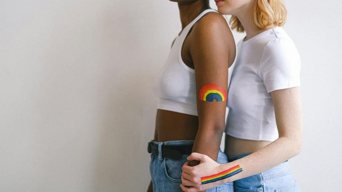 A close embrace between an interracial couple with rainbow body art symbolizing LGBTQ pride.