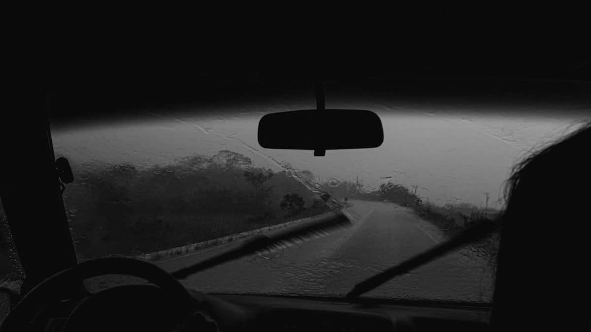 View from a car interior during a rainy drive on a wet road, captured in grayscale.