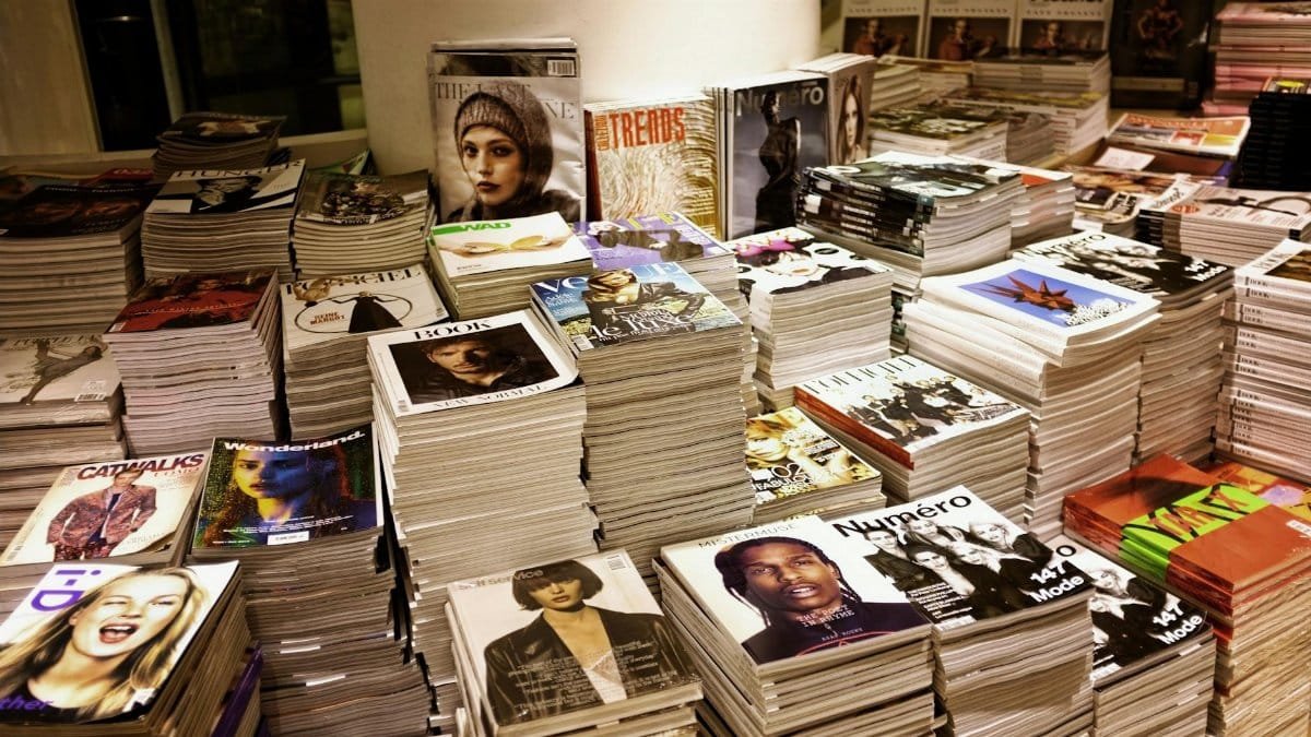 Huge stacks of diverse fashion and lifestyle magazines piled high in an indoor store setting.