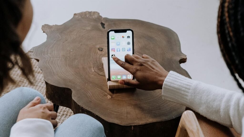 Two individuals use a smartphone together indoors, focused on screen interaction on a wooden table.