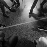 Black and white photo of a support group session indoors with diverse participants.