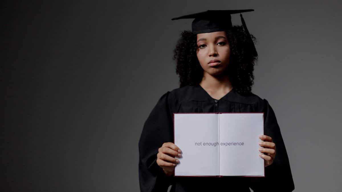 Young graduate holding a book with 'not enough experience' message, symbolizing job hunt difficulties.