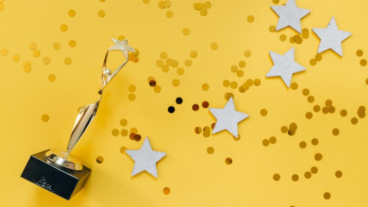 Shiny golden trophy and stars on a vibrant yellow background, symbolizing success and victory.