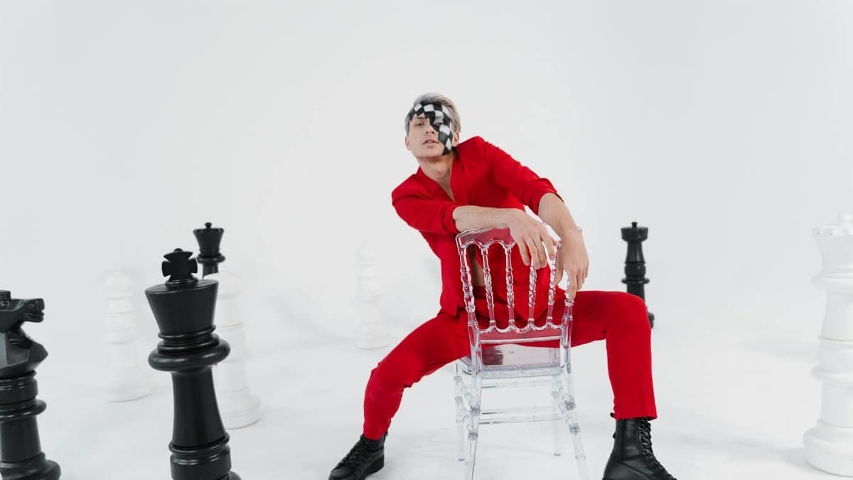 A creative fashion photo featuring a person in red among giant chess pieces on a white background.