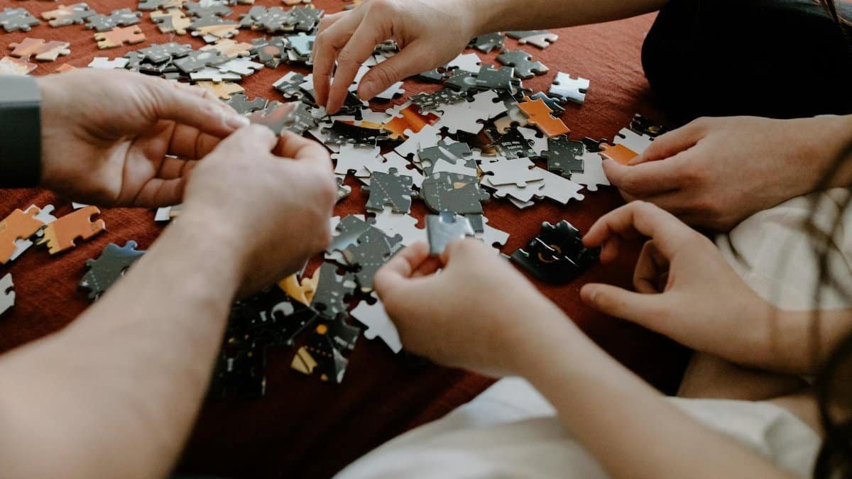 Close-up of multiple hands working together to solve a puzzle on a table indoors.