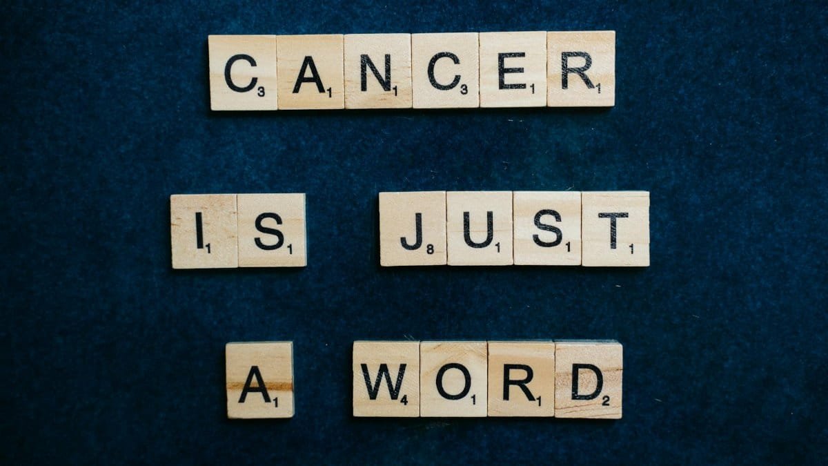 Scrabble tiles spelling 'Cancer is just a word' on a blue background promoting hope and support.